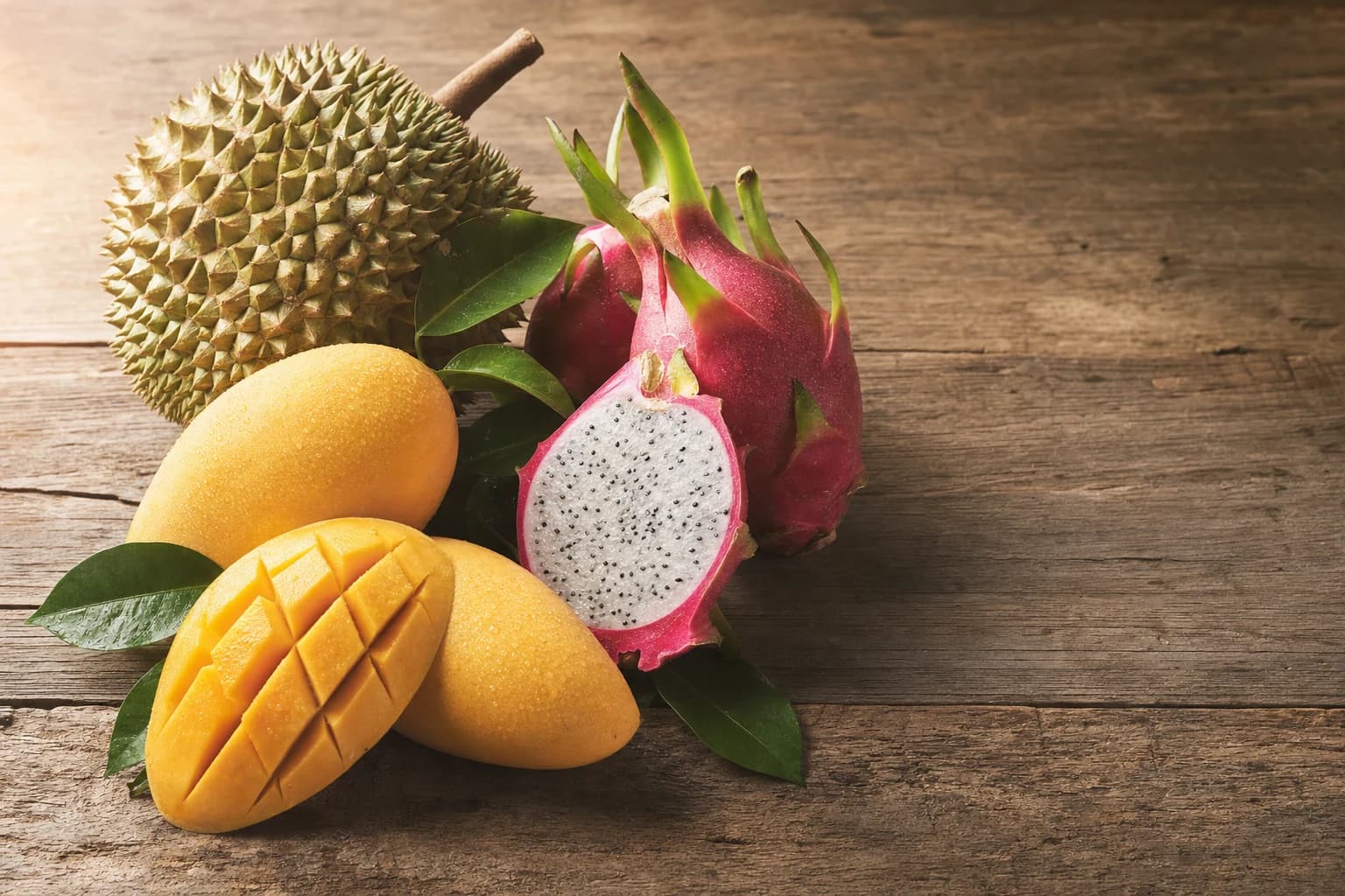 Fresh Vietnamese durian, dragon fruit halved, and ripe mangoes arranged on a rustic wooden table